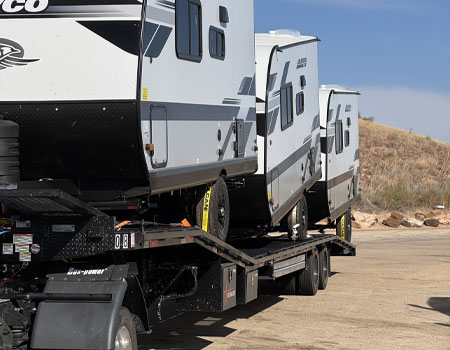 Multiple RVs loaded on an open trailer, securely fastened for safe door-to-door RV transport services