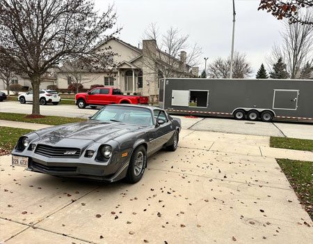Classic Camaro being delivered on a residential driveway from an enclosed trailer, highlighting door-to-door enclosed auto transport services
