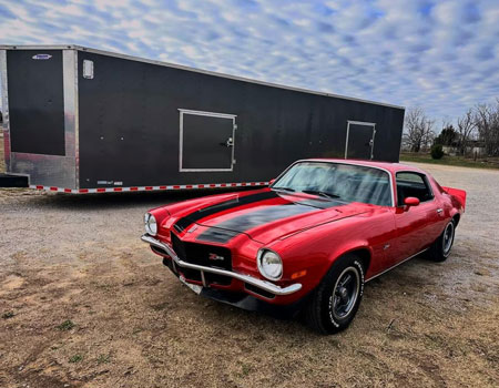 Classic Camaro parked in a residential driveway with an enclosed trailer in the background, delivered using enclosed auto transport services