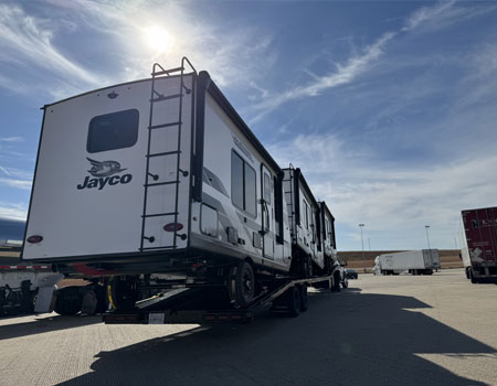 Three RVs securely strapped on an open trailer, prepared for door-to-door delivery through professional RV transport services
