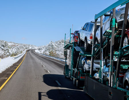 Car carrier truck driving on a snowy mountain road, representing seasonal challenges in nationwide auto transport services