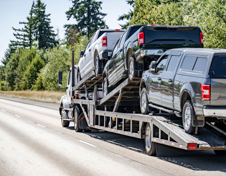 Open car carrier hauling three trucks, providing open auto transport services across the U.S.